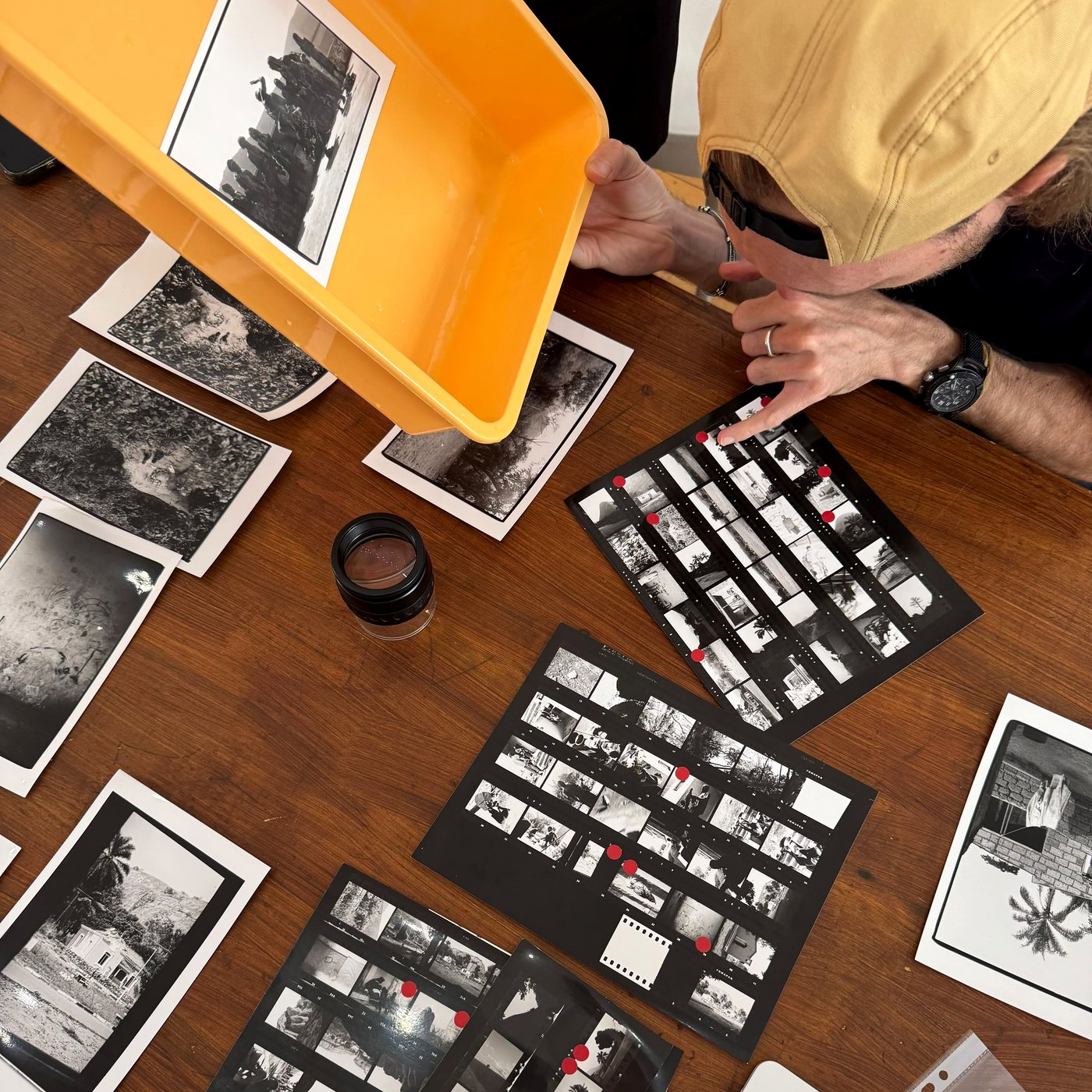Checking contact sheets and prints at the lab table with a loupe and a tray of prints