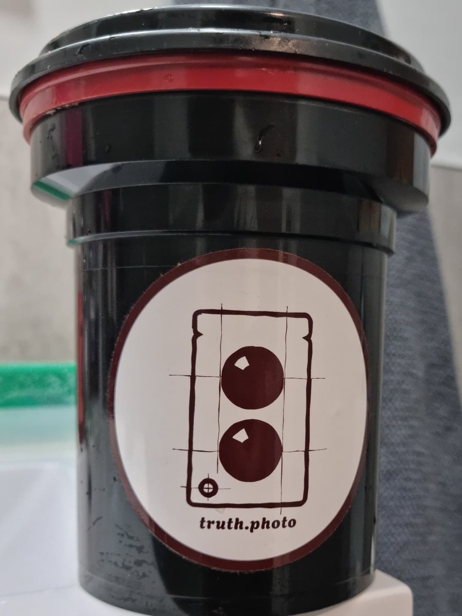 A black film developing tank with a red ring and a round sticker on its side