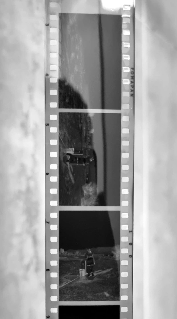 A strip of developed 35mm film hanging against a wall, with each frame visible