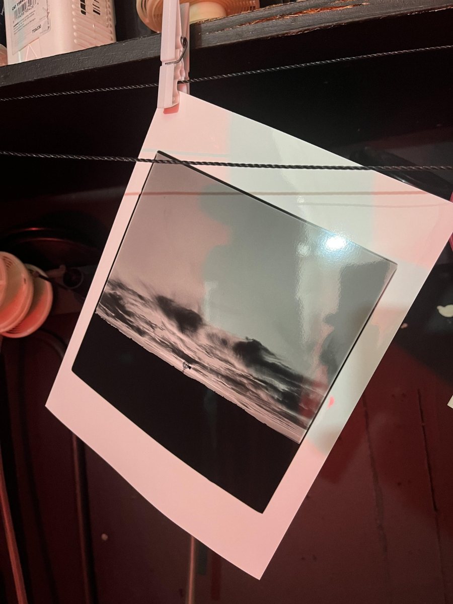 A black and white print hanging from a clothes peg on a drying line in the red light of the darkroom